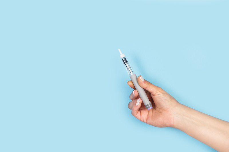 Woman holding an insulin injection pen on a light blue background with copy space